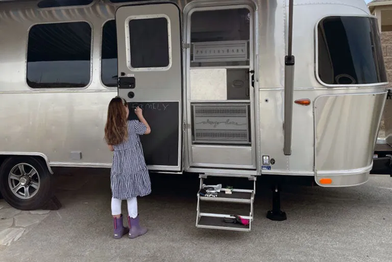 Child at the door of a silver travel trailer