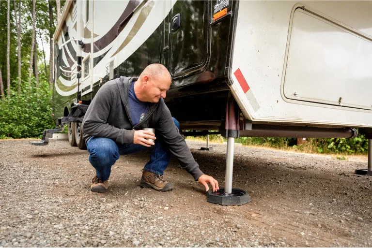 Man crouching beside a motorhome jack fitted with a SnapPad on gravel
