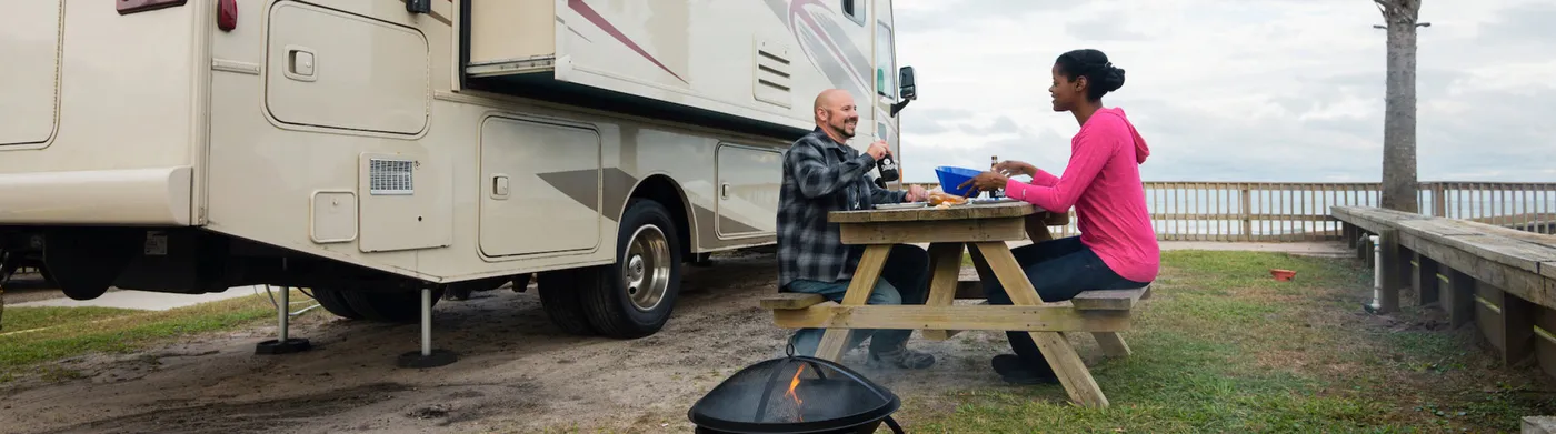Couple at a picnic table beside their fifth wheel by the water